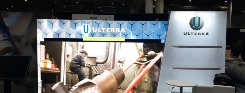 Ulterra trade show booth. AVR Expos video wall. Video shows worker operating equipment. Modern design with Ulterra logo and branding on panels and banners. Good lighting and layout. People walking by.󠁧󠁢󠁳󠁣󠁴󠁿