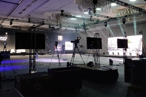 The photo depicts an indoor event setup with professional AV equipment, showcasing the capabilities of AVR Expos. The scene includes large screens, cameras, lighting rigs, and other audiovisual equipment strategically placed to capture and display high-quality video and audio. We carry the latest AV rentals in Dallas for events like this.
