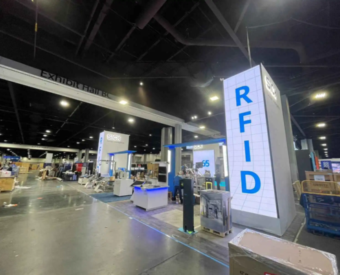 The photo captures a section of an exhibition hall during setup. Prominently featured is a large, modern booth for a company specializing in sensor intelligence and RFID technology. The booth includes tall, well-lit structures with LED Screen rentals provided by AVR Expos showcasing the company's branding and technology focus.