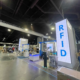 The photo captures a section of an exhibition hall during setup. Prominently featured is a large, modern booth for a company specializing in sensor intelligence and RFID technology. The booth includes tall, well-lit structures with LED Screen rentals provided by AVR Expos showcasing the company's branding and technology focus.