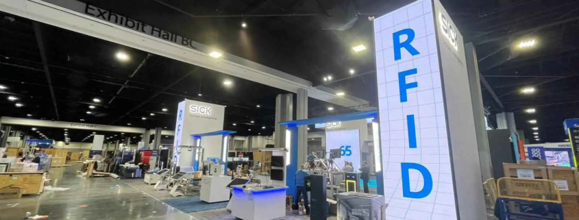 The photo captures a section of an exhibition hall during setup. Prominently featured is a large, modern booth for a company specializing in sensor intelligence and RFID technology. The booth includes tall, well-lit structures with LED Screen rentals provided by AVR Expos showcasing the company's branding and technology focus.