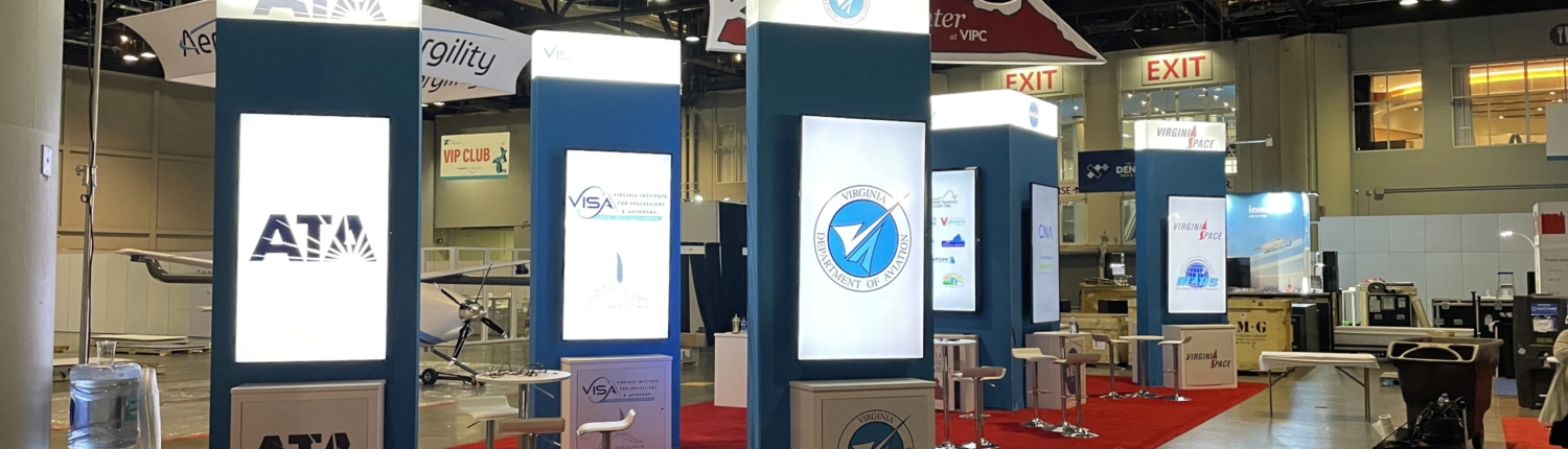 Trade show booth featuring interactive touchscreen monitors displaying engaging content, with attendees interacting and navigating through digital displays in a professional event space.