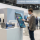 Trade show attendee using a touchscreen next to a physical product display in a hybrid demo booth.