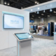 Minimalist trade show booth using a single large monitor and touchscreen to reduce AV rental costs.